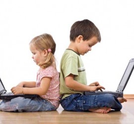 Una niña y un niño pequeño cada uno con un portatil apollandose en sus espaldas mutuamente